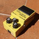 Žlutý efekt pedál s černým nášlapem. Na horní části je nápis SUPER OverDrive SD-1 a šipky s označením INPUT a OUTPUT. Na přední straně jsou tři černé…