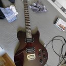 Tmavě červená elektrická kytara s tmavým hnedým hmatníkem a stříbrným hardwarem. Nástroj má dva humbuckery, čtyři ovládací knofíky a fixní most. Na h…
