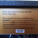 Fotografie detailu zlatého štítku na hudebním přístroji. Na štítku je text: MODEL 8080 SOLID STATE LEAD AMPLIFIER, 80 Watts RMS / 8 ohm. Dále následu…