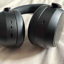Černá bezdrátová sluchátka s hlavovým obloukem. Na levém sluchátku jsou vidět dva USB-C porty a malý otvor pro mikrofon. Povrch je matný, bez viditel…