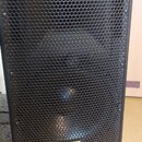 Černý reproduktor v bedně s kovovou perforovanou mřížkou. V dolní části mřížky je žlutý obdélníkový štítek s nápisem SPL Acoustics. Povrch bedny má s…