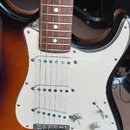Elektrická kytara s trupem v barvě sunburst a bílým pickguardem. Na hmatníku z tmavého dřeva jsou vidět bílé tečkové značky. Nástroj má tři snímače t…