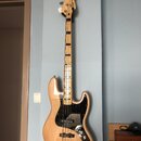 Elektrická basová kytara s přírodním dřevěným povrchem těla a hmatníkem. Tělo má černý pickguard a na hlavě je viditelné logo "Squier". Nástroj vykaz…