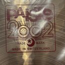 Detailní záběr na povrch mosazného činele s červeným potiskem. V rámečku je uveden nápis PAISTE, pod ním modelové označení 2002 a text TRADE MARK MAD…