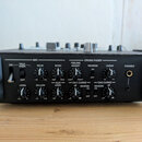 Černý DJ mixér s řadou ovládacích prvků. Na předním panelu jsou nápisy MIC, CROSS FADER, TALK OVER, LEVEL, EQ HI, EQ LOW, ECHO, AUX LEVEL, FEELING AD…