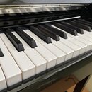 Detailní pohled na klávesnici pianina s černým lakovaným povrchem. Jsou vidět bílé a černé klávesy v dobrém stavu bez výrazného opotřebení. V horní č…