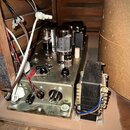 Fotografie zachycuje vnitřní část elektronického zařízení s vakuovými elektrónkami a transformátorem. Na kovovém šasi je vidět varovný nápis: „CAUTIO…