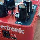 Červený kytarový efekt s nápisem tc electronic. Na přední straně jsou čtyři černé oválné ovladače a jeden malý přepínač. V dolní části je uveden nápi…