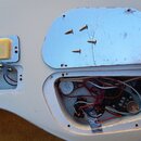 Fotografie zachycuje zadní stranu bílé elektrické kytary s vyjmutými kryty elektroniky. V dutinách je vidět zapojení kabelů, potenciometry a baterie…