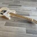 Elektrická kytara s přírodním dřevěným povrchem těla a bílým pickguardem. Na hlavě hmatníku je čitelné logo Fender a nápis Telecaster. Nástroj vykazu…
