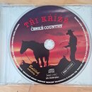 Fotografie znázorňuje kompaktní disk (CD) v průhledném plastovém obalu. Na povrchu disku je červeně-modrý grafický motiv s siluetami koně a kovboje a…