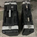 Dvě černé obdélníkové transportní skříně z texturovaného materiálu s hliníkovými hranami a zapínacími zámky. Na levé skříni je vidět čtvercové logo s…