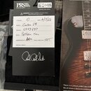 Fotografie zachycuje bílý štítek s technickými údaji, který je připevněn k černému povrchu. Na štítku je logo PRS PAUL REED SMITH GUITARS a nápisy: S…