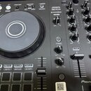 Černý DJ kontrolér s velkým stříbrno-šedým jog-colem. Na horní části je nápis PERFORMANCE DJ CONTROLLER DDJ-FLX4 a loga rekordbox a serato. V pravém…