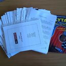 Na fotografii je hromada papírových listů s notami a jedna kniha. Na předním listu je nápis SKY GUITAR, Level 1 a 12 Essential Songs. Modrá kniha nes…