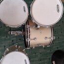 Sada bubnů v béžové barvě se třpytivým povrchem. Na blanách jsou viditelná loga EVANS. V horní části je umístěn velký basový buben a dva menší tom-to…