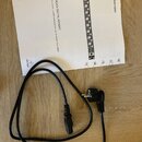 Na fotografii je černý napájecí kabel s klasickým síťovým konektorem a přiložený papírový návod. Na návodu je nápis Quick Start Guide, název modelu U…