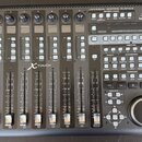 Černá kontrolní plocha s nápisem UNIVERSAL CONTROL SURFACE ENCOVER ROSSIGN a logem behringer. Zařízení obsahuje osm posuvníků, řadu tlačítek s různým…