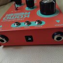Červený efekt pedál s modrými detaily. Na horní ploše jsou nápisy dre:adbox, KOMO REEBI a popisky konektorů LFO OUT, RATE, STATIC, INPUT a OUTPUT. Na…