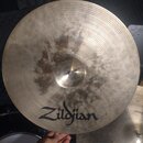Kruhový kovový činel zlatavé barvy s viditelným broušením v koncentrických kruzích. Na spodní části je černý nápis Zildjian. Povrch činelu vykazuje v…