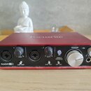 Červené audio rozhraní značky Focusrite. Na předním panelu jsou dva vstupy s knoflíky označenými jako GAIN 0 10 a přepínači LINE INST. V pravé části…