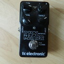 Černý kytarový efekt s nápisy GAIN, VOICE, BASS a TREBLF u ovládacích knoflíků. Uprostřed je bílý nápis DARK MATTER DISTORTION a v dolní části značka…