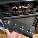 Černý obdélníkový ovladač s čtyřmi kovovými potenciometry a jedním přepínačem. Na zařízení jsou bílé nápisy CHANNEL, GAIN, CLEAN BOOST a REVERB/EFFEC…