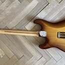 Zadní strana elektrické kytary s dřevem v odstínech hnědé a žluté (sunburst). Na zadní straně krku je nápis "SN: 10528787" a pod ním menší, nečitelný…