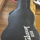 Černý tvrdý kufýr na kytaru s texturovaným povrchem. Na spodní části je bílý nápis Gibson USA. Povrch vykazuje drobné oděrky a nečistoty.