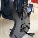 Černá elektrická kytara s matným povrchem umístěná na černém stojanu. Nástroj má dva humbuckery, jeden ovládací knoflík a přepínač. Na hmatníku jsou…