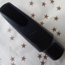 Černý, hladký dutý nástavce (mundstück) z plastu nebo ebonitu. Na povrchu je viditelný vodoznak s nápisem saxofonservis.eu. Předmět vykazuje mírné zn…
