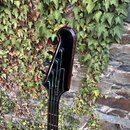 Detail hlavy tmavě hnědé basové kytary s černými ladicími kolíky. Na čele hlavy je bílý nápis Epiphone a modré dekorativní linky. Povrch laku je glos…