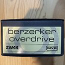 Fotografie znázorňuje horní část krabičky od efekt pedálu v tmavě modré barvě. Na vrchu je nalepený světle zelený štítek s nápisy „berzerkerken overd…