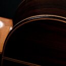 Detailní záběr na korpus akustické kytary z tmavého dřeva s výraznou sletovanou strukturou. Okraje jsou zdobeny světlým lemováním. Povrch je lakovaný…