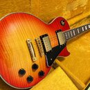 Elektrická kytara s trupem ve tvaru single-cut a povrchem v červeno-žlutém přechodu (sunburst) s viditnou strukturou dřeva. Nástroj má dva humbuckery…
