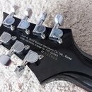 Záběr na hlavu černé elektrické kytary s chromovanými ladičkami. Na zadní straně hlavy je bílý nápis: „Built by World Musical Instrument Co. Ltd., Ko…