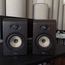 Dva studiové monitory v tmavě hnědém dřevěném provedení s rounded hranami. Každý reproduktor má v horní části výšek s černou mřížkou a ve spodní část…
