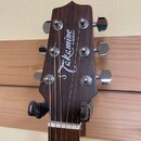 Fotografie zachycuje hlavu akustické kytary z tmavého dřeva s kovovými ladičkami. Na povrchu je bílý nápis Takamine a vedle něj menší text G SERIES.…