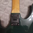 Detail krku a spoje s tělem elektrické kytary v tmavě zelené barvě. Na černé plastové krytce spoje je vyražené logo Kramer, pod ním kód S 1220 a dále…