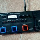 Černý kytarový procesor s nápisem BOSS GT-1 GUITAR EFFECTS PROCESSOR. Zařízení má digitální displej, na kterém je text TERA ECHO LEAD a další ovládac…