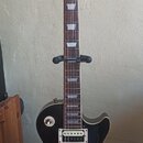 Elektrická kytara typu Les Paul s barevným přechodem od žluté přes oranžovou k hnědé (sunburst). Na hlavě je bílý nápis Epiphone a zlatý nápis Les Pa…