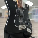 Černá elektrická kytara s tvarem typu Stratocaster a černým pickguardem. Nástroj má tři snímače, tři ovládací knofíky a dřevěný hmatník. Povrch lakov…