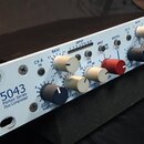 Bílý rackový kompresor s nápisem 5043 Portico Series Duo Compressor. Zařízení má dva identické kanály ovládacími knoflíky v barvách modré, krémové a…