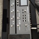 Šedý kytarový procesor s černým displejem a expresním pedálem. Na přístroji je nápis BOSS GX-100 GUITAR EFFECTS PROCESSOR a logo AIRD. Jsou zde vidit…