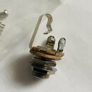 Fotografie zachycuje malý kovový elektronický komponent, pravděpodobně potenciometr nebo přepínač. Součást má stříbrné a zlatavé kovové povrchy s vid…