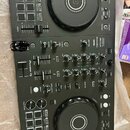 Černý DJ kontrolér s dvěma jog-koly, faderem a řadou tlačítek a knoflíků. Na levé straně je svisle napsáno logo Pioneer DJ. Povrch vykazuje běžné zná…