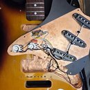Elektrická kytara s korpusem v barevném přechodu od žluté přes oranžovou k hnědé. Kytara má černý pickguard, pod kterým je viditelná měděná stínění a…
