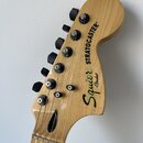 Fotografie zachycuje hlavu elektrické kytary z přírodního světlého dřeva. Na povrchu je černý nápis Squier by Fender a STRATOCASTER®. Nástroj má šest…