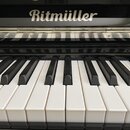 Detailní pohled na klávesnici černého pianina. Na černé horní části je bílý nápis Ritmüller. Klávesy jsou v dobrém stavu, bez viditelného opotřebení.