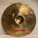 Zlatavý mosazný činel s viditelným kovánívým povrchem. Ve spodní části je červený nápis „Masterwork“ a pod ním menší text „Handmade in Turkey“. V hor…